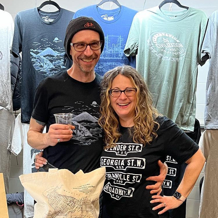 Two people standing in a store with t-shirts hanging on the wall behind them.