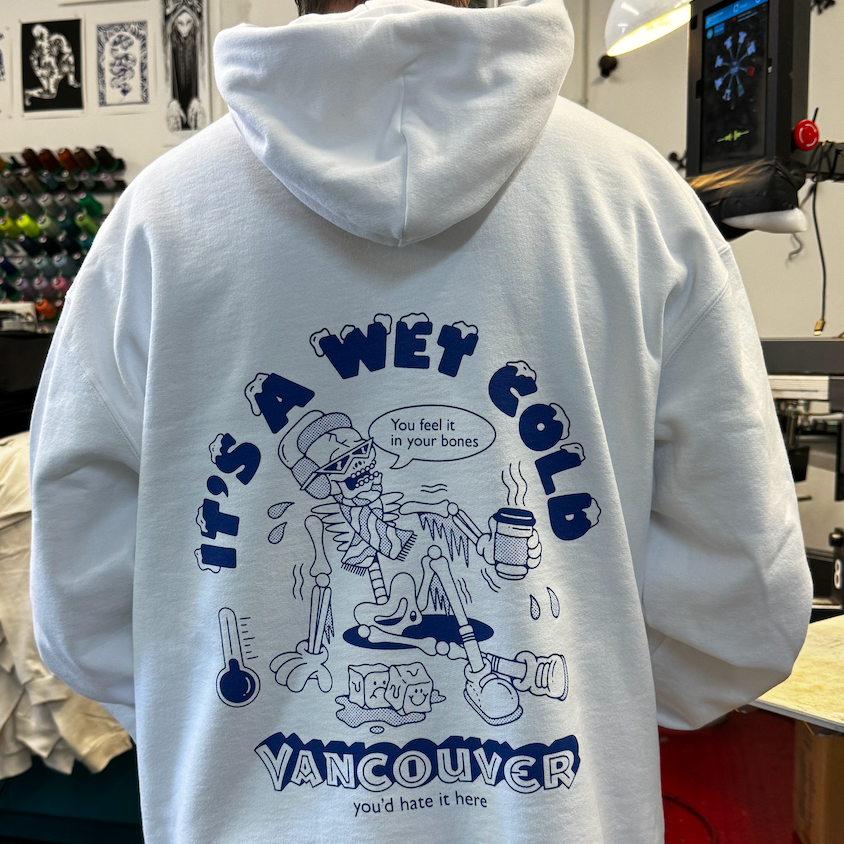 White hoodie with blue graphics and text on the back, worn by a person in an indoor setting.